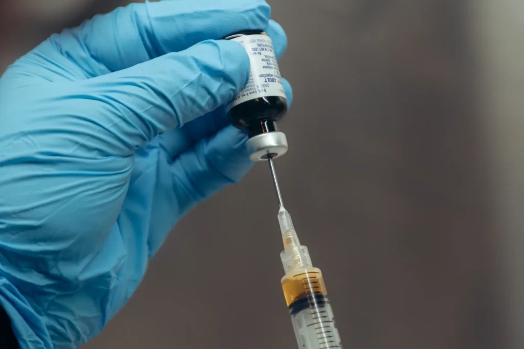 Gloved hands drawing a dose from a vial into a syringe